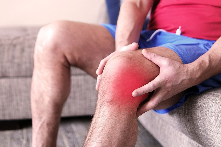 A man on a couch clutching his knee in excruciating pain. Joint pain, arthritis and tendon...