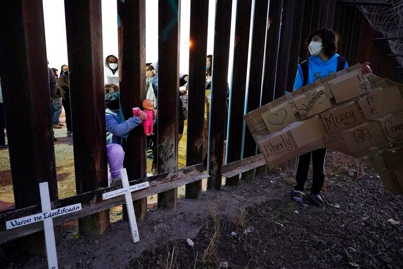 Una niña en México mete su muñeca entre las barreras de la valla fronteriza de Estados...
