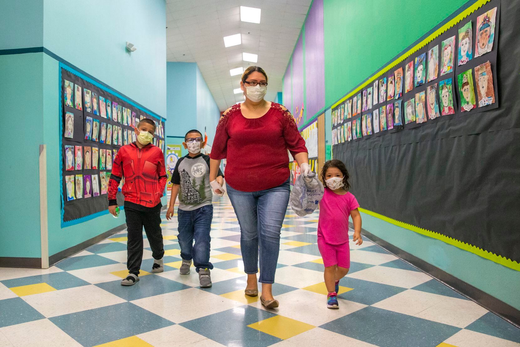 Angie Andrade (center) and her children (from left) Angel, 10, Austin, 7, and Abigail, 3, wear face masks as they walk to pick up sack lunches at J.T. Saldivar Elementary School during spring break. DISD will move to drive-through style pickups as the district continues to provide meals to students amid closures.