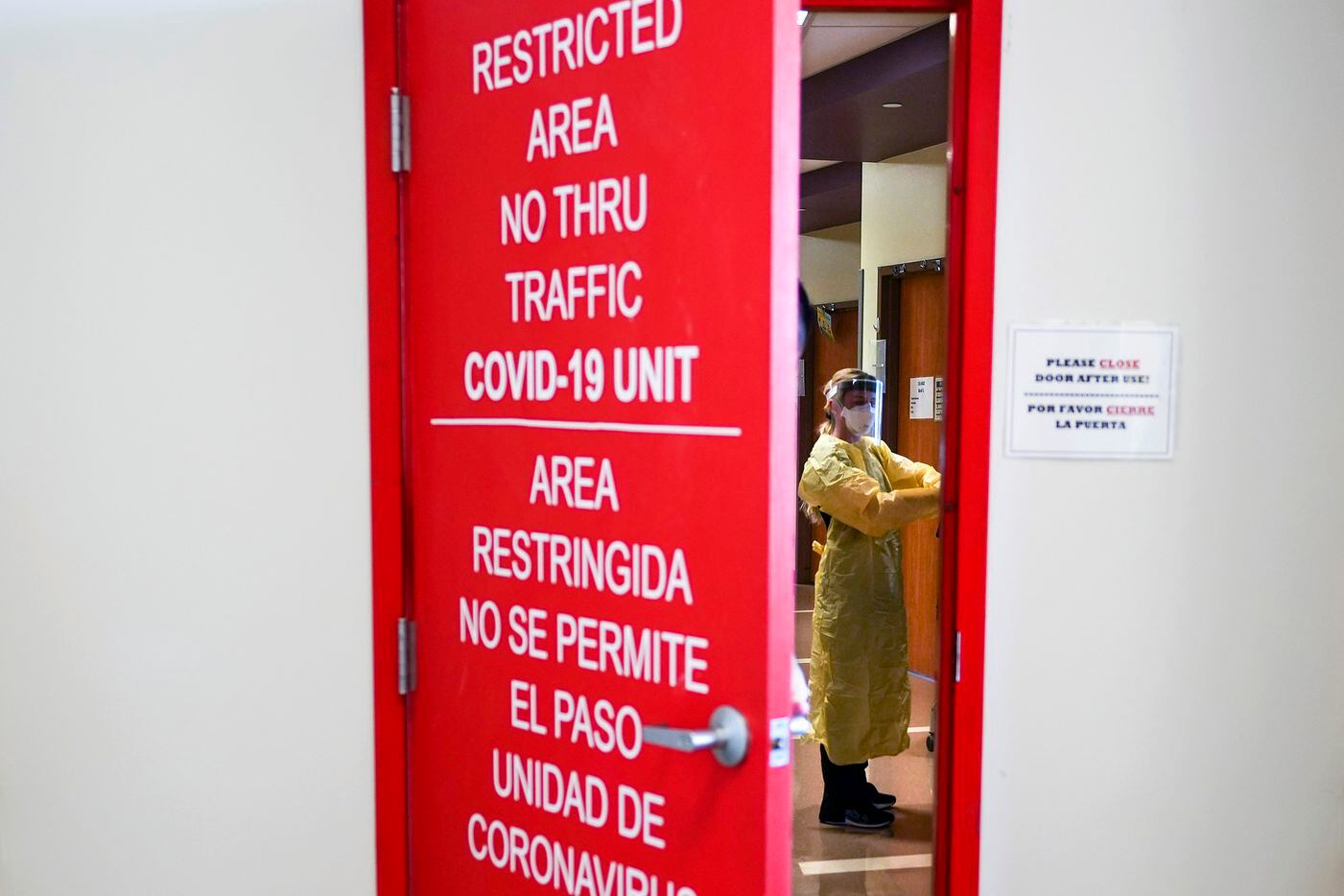 Nurses can be seen working the hallway as a red door covered with restrictive warnings is closed on the COVID-19 unit at Parkland Hospital on Wednesday, Jan. 5, 2022, in Dallas.