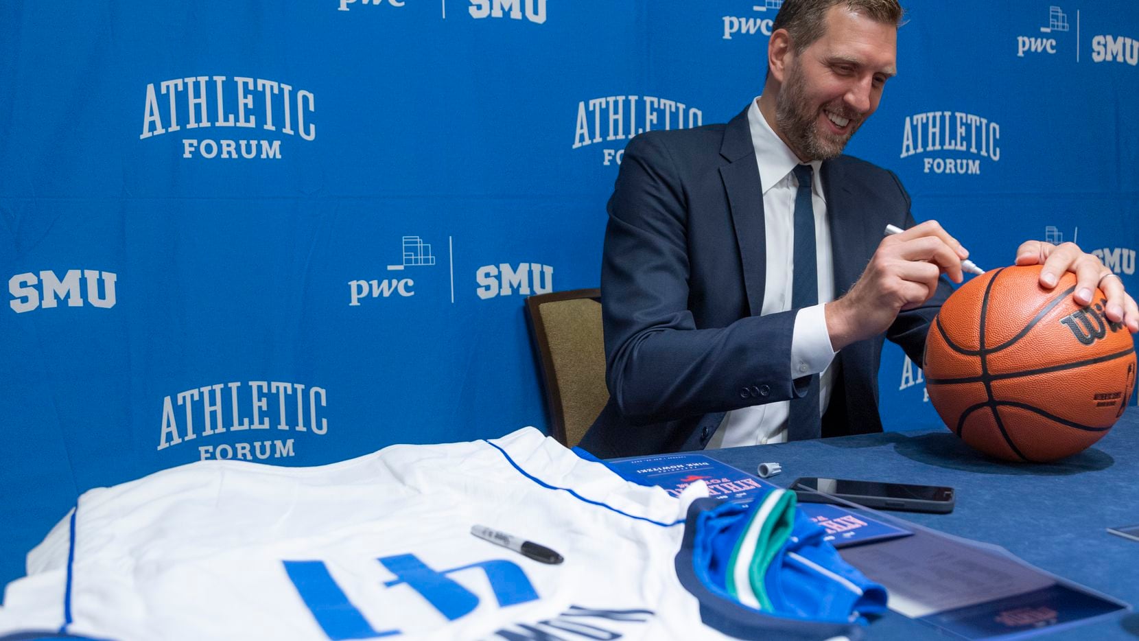 Former Dallas Mavericks player Dirk Nowitzki autographs a basketball before speaking at the...