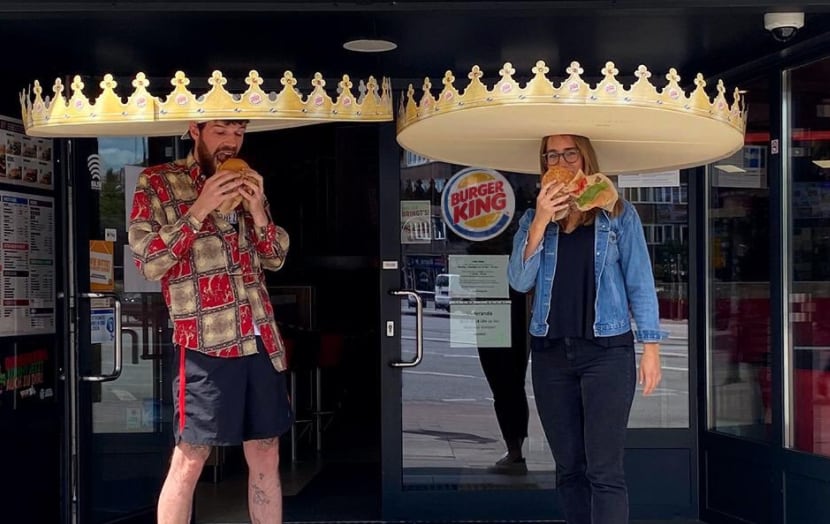 Imagen de Burger King donde se ve a dos personas comiendo hamburguesas y portando sus...