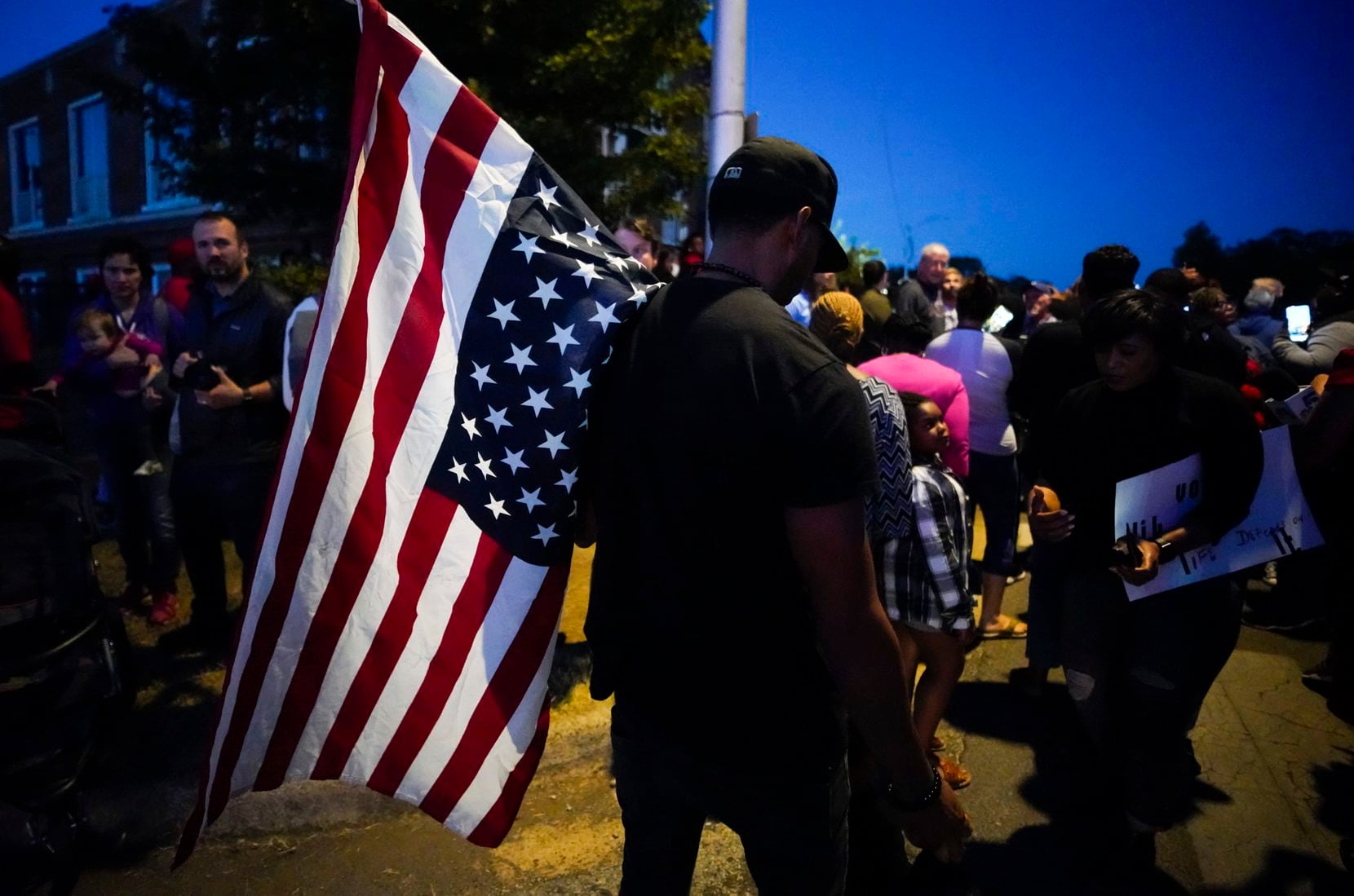 A large crowd of protestors, including a man carrying an upside-down American flag, gathered...