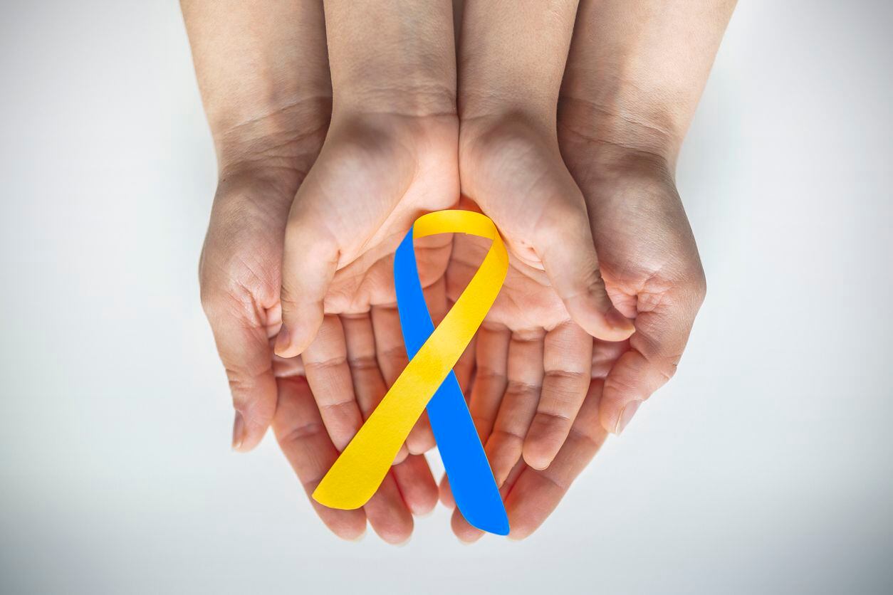 Adult and child hands holding blue and yellow ribbon shaped paper. March 21 is World Down...