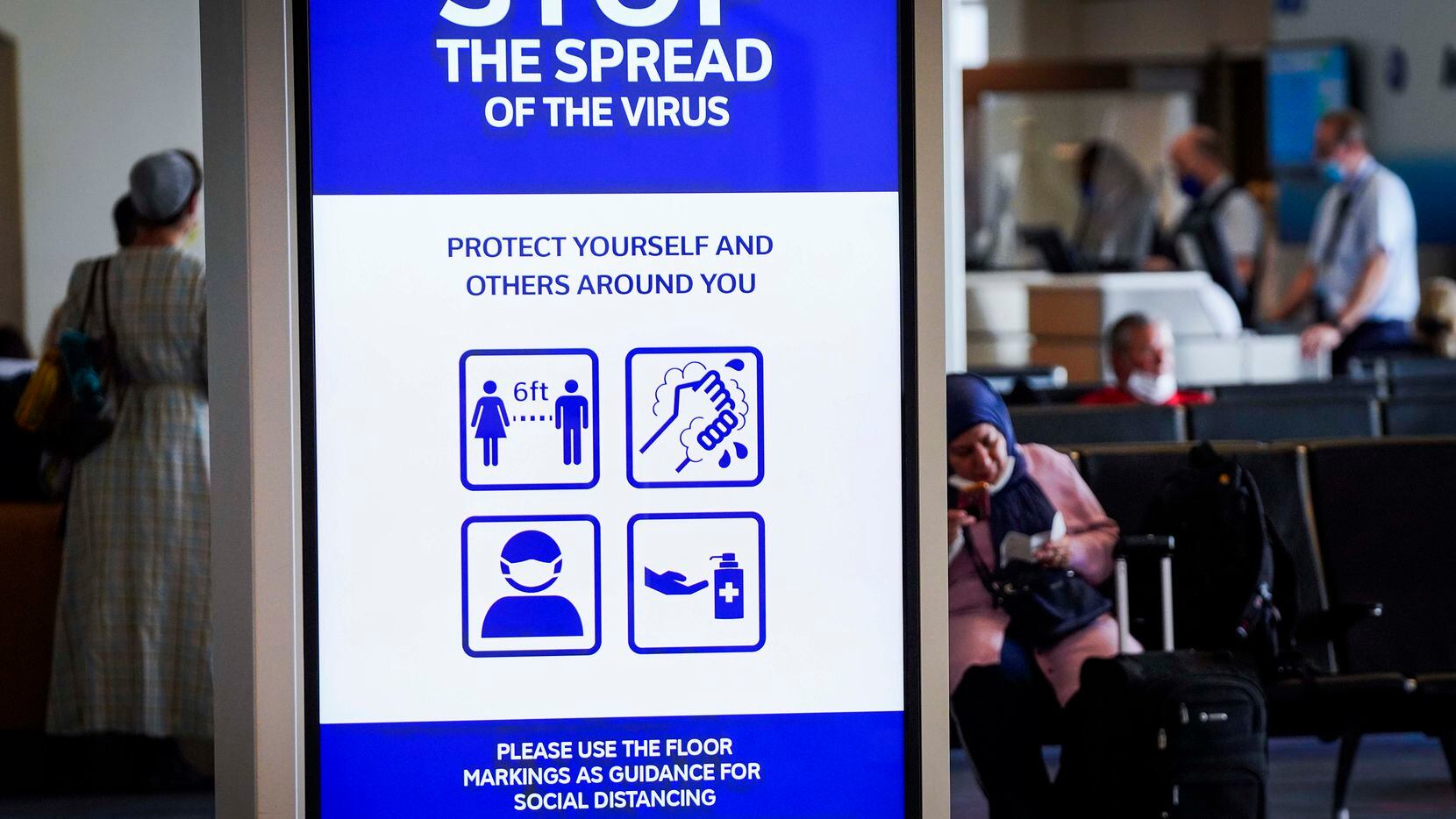 A message board displayed a public health notice of precautions against the spread of COVID-19 as passengers waited to board an American Airlines flight at DFW International Airport Terminal A on June 30, 2020.