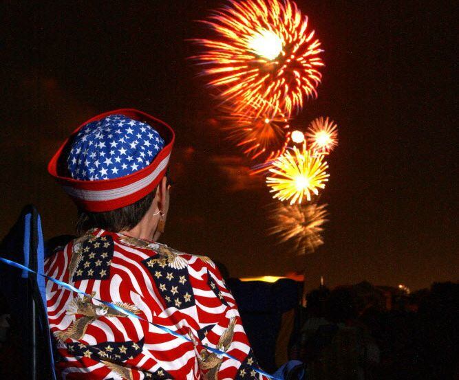 A woman in a patriotic shirt watches fireworks at Carrollton/Farmer Branch ISD athletic...