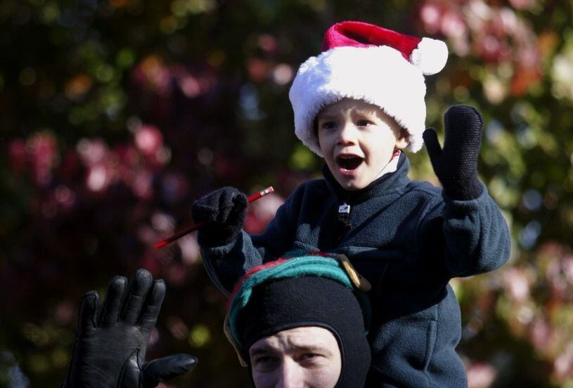 A boy waves while watching a Christmas parade from his father's shoulders.