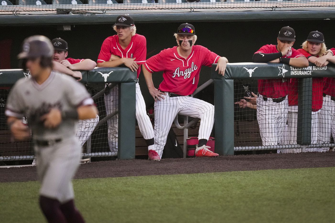 Argyle players look on from the dugout as Sinton shortstop Blake Mitchell heads for home to...