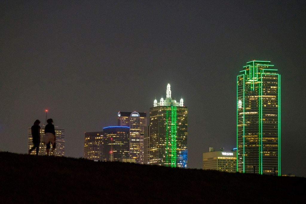 The downtown skyline lights up behind walkers on the Trinity Skyline Trail on Thursday,...