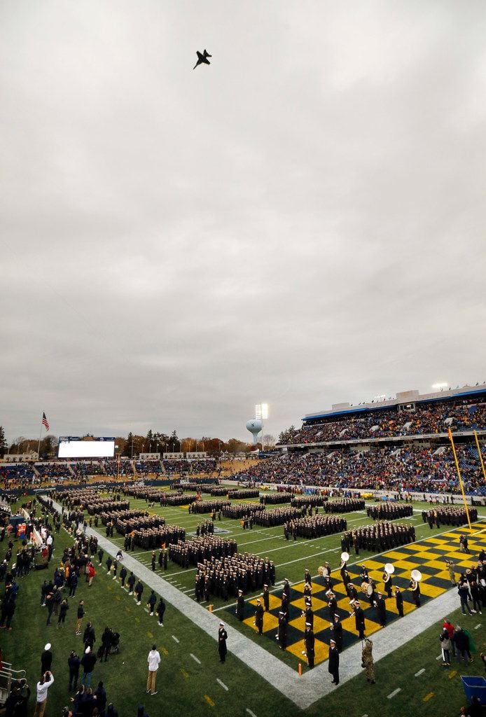 A military aircraft performs a flyover as Navy Midshipmen line the field during the national...