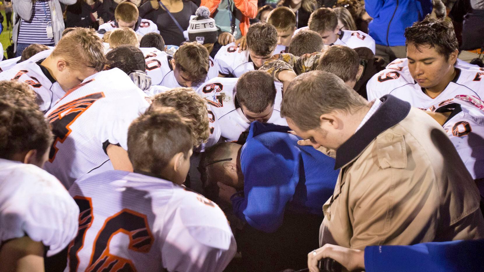 Bremerton High School assistant football coach Joe Kennedy (center in blue) kneels and prays...