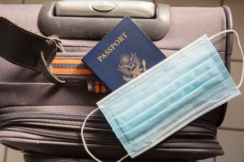 Un pasaporte de Estados Unidos junto con una mascarilla y una maleta de viaje.