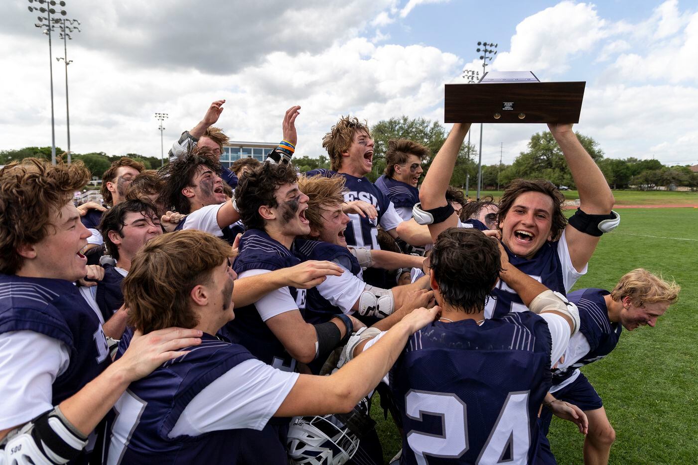 Episcopal School of Dallas’ Eli Huggins holds the trophy as his team celebrates a 14-5 win...