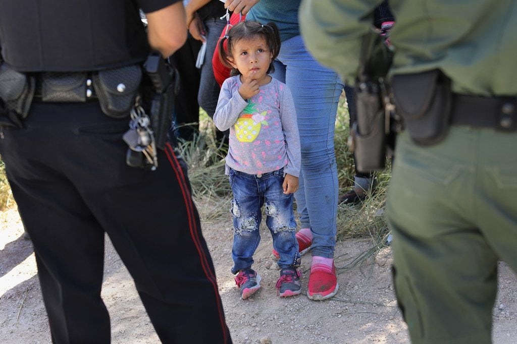 A Mission Police Dept. officer and a U.S. Border Patrol agent watch over a group of Central American asylum-seekers before taking them into custody on June 12, 2018 near McAllen. Local police officers often coordinate with Border Patrol agents in the apprehension of undocumented immigrants near the border. The immigrant families were then sent to a U.S. Customs and Border Protection processing center for possible separation.