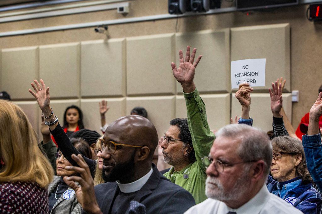 People raise their hands and one citizen holds up a "No expansion of CPRB" sign as the...