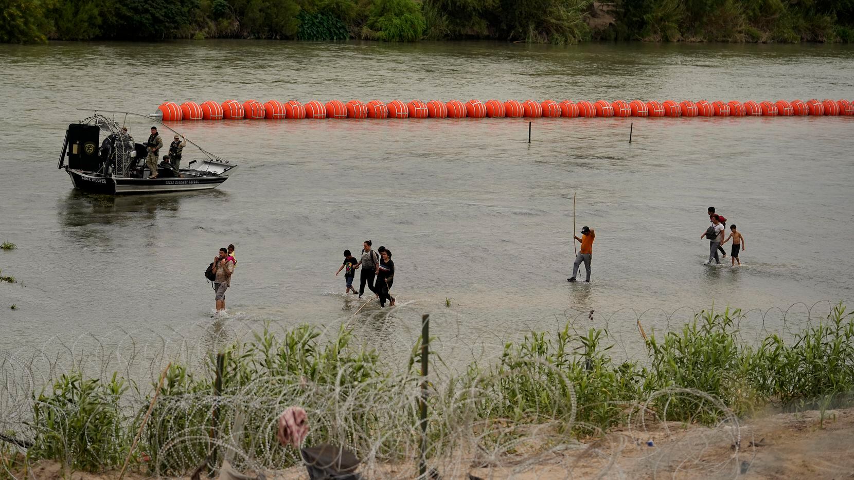 Migrantes que cruzaron el Río Grande desde México pasan por la barrera de boyas colocada por...