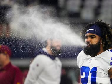 Dallas Cowboys running back Ezekiel Elliott blows water while warming up before an NFL...