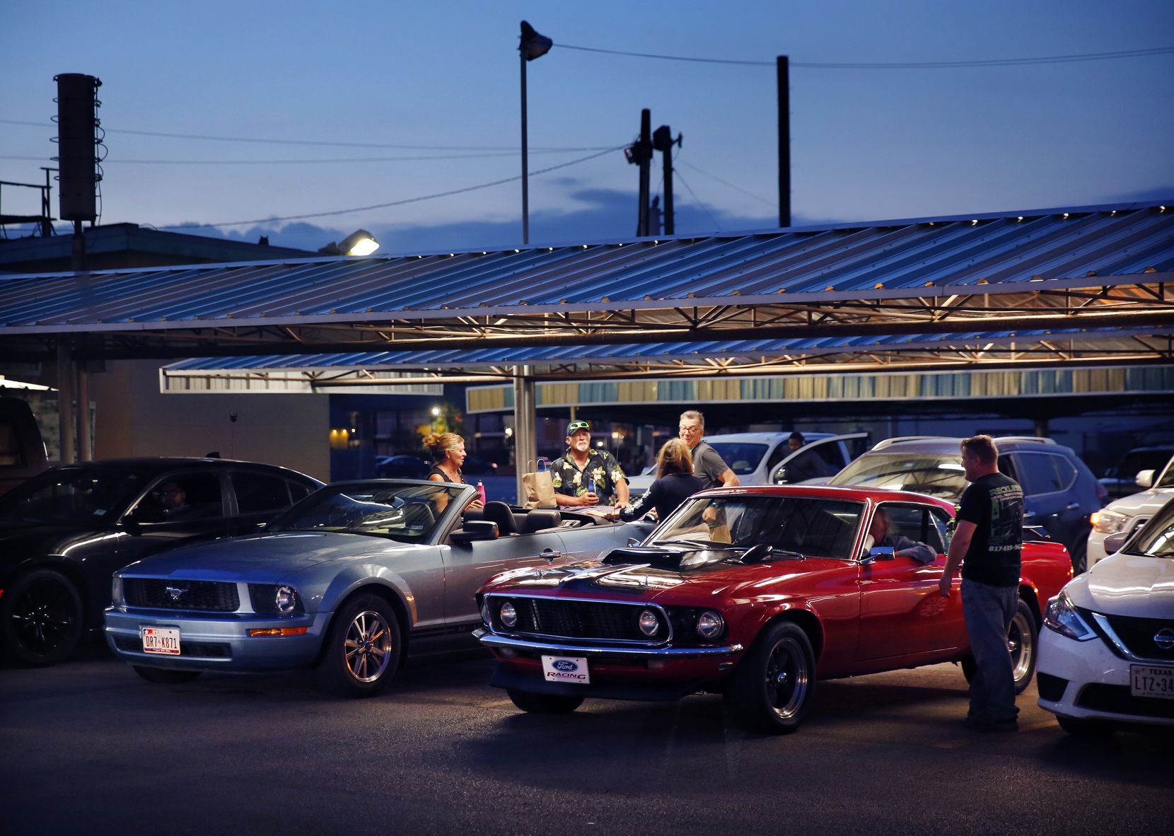At dusk, people visit around a pair of Ford Mustangs at Keller's Drive-In. The burger and...