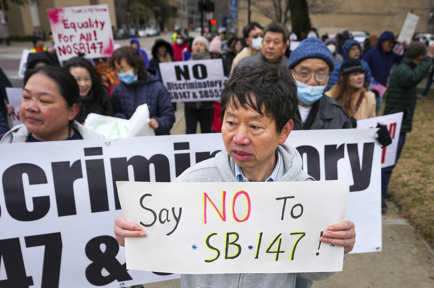 Hank Huang holds a sign reading “Say No To SB-147” as demonstrators march in opposition to...