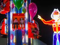 Neon Big Tex points toward youngsters on a ride on the midway on opening night at the State...