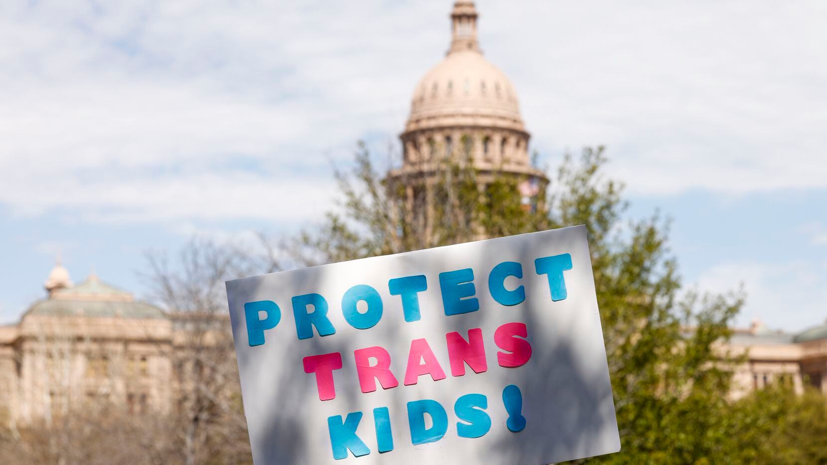 An attendee raises a “Protect Trans Kids” sign in front of the Texas State Capitol during...