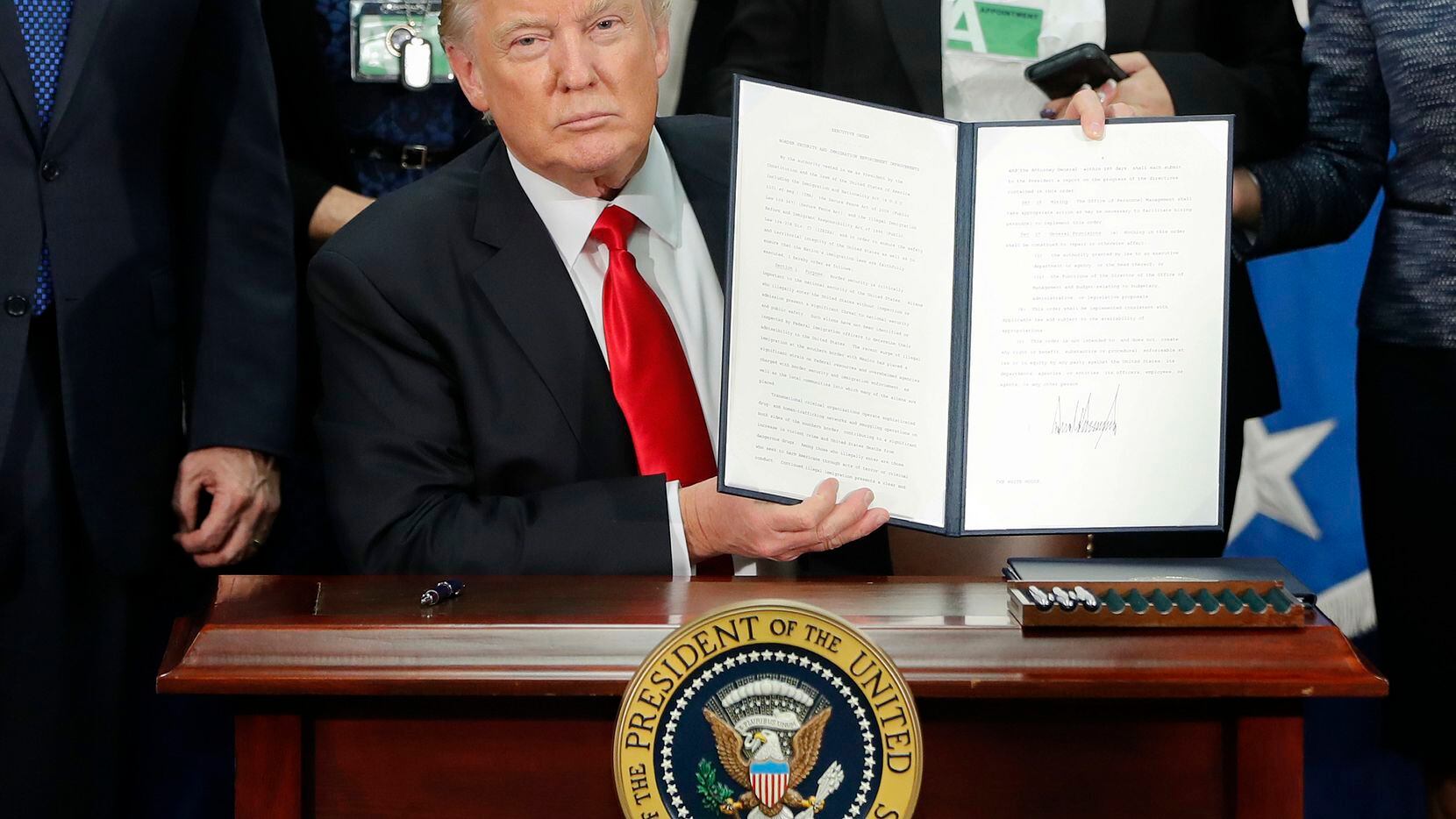El presidente Donald Trump sostiene el documento de orden ejecutiva respecto a reforzamiento de la frontera y restricciones de visas, el 25 de enero de 2017.