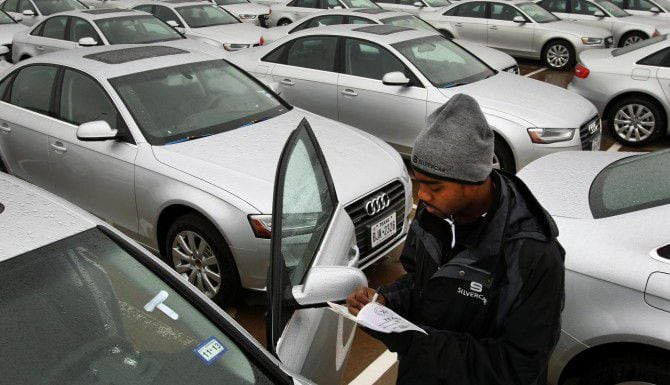 Un empleado de una agencia de renta de vehículos inspecciona un auto recién entregado....