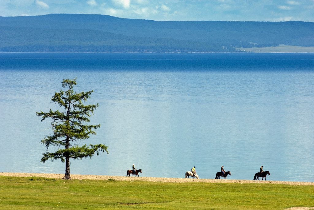 Riders on horseback explore the edge of Lake Hovsgol, the largest freshwater lake Mongolia,...