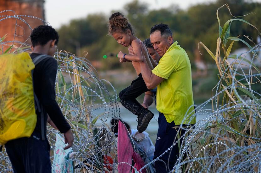 A young girl is lifted over concertina wire are she and other other migrants crossed the Rio...