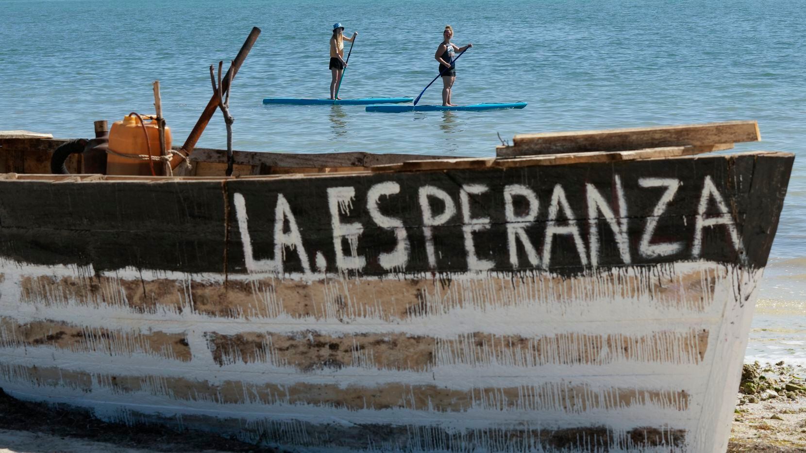 Paddleboarders draw close to get a better look at a beached migrant boat named "La...