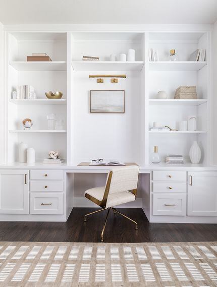 White built-in wall bookshelves around a home workspace, filled with decor, and books, with...