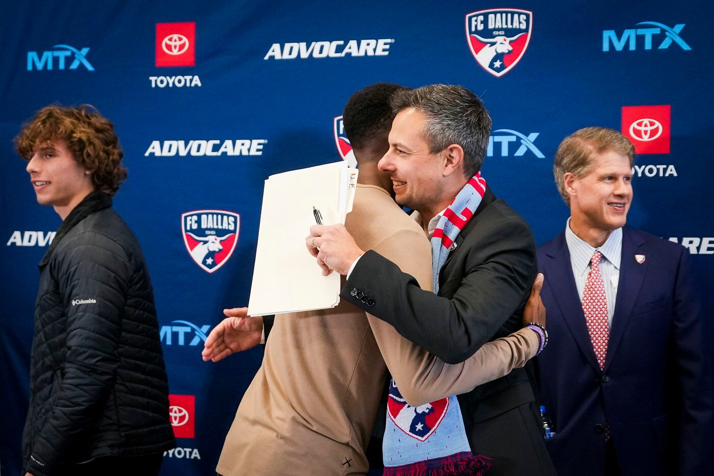 New FC Dallas head coach Nico Estévez (facing) hugs defender Edwin Munjoma after his introductory press conference at the National Soccer Hall of Fame on Friday, Dec. 3, 2021, in Frisco, Texas. Forward Benjamin Redžic is at left and team chairman and CEO Clark Hunt.