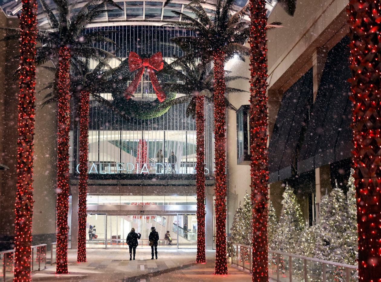 Shoppers walk through the pathway of palm trees and falling snow during a snow...