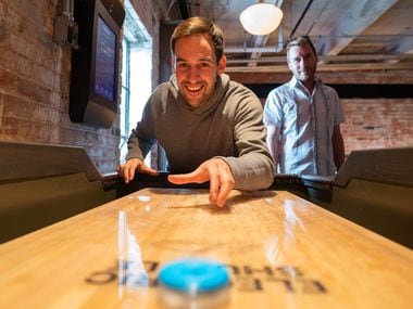 Gene Ball, CEO of Electric Shuffle USA, left, and Stephen Moore, CEO and founder, demonstrate how to use the modern shuffleboard tables and video board at Electric Shuffle in Dallas' Deep Ellum. The bar is expected to open Nov. 19, 2021.