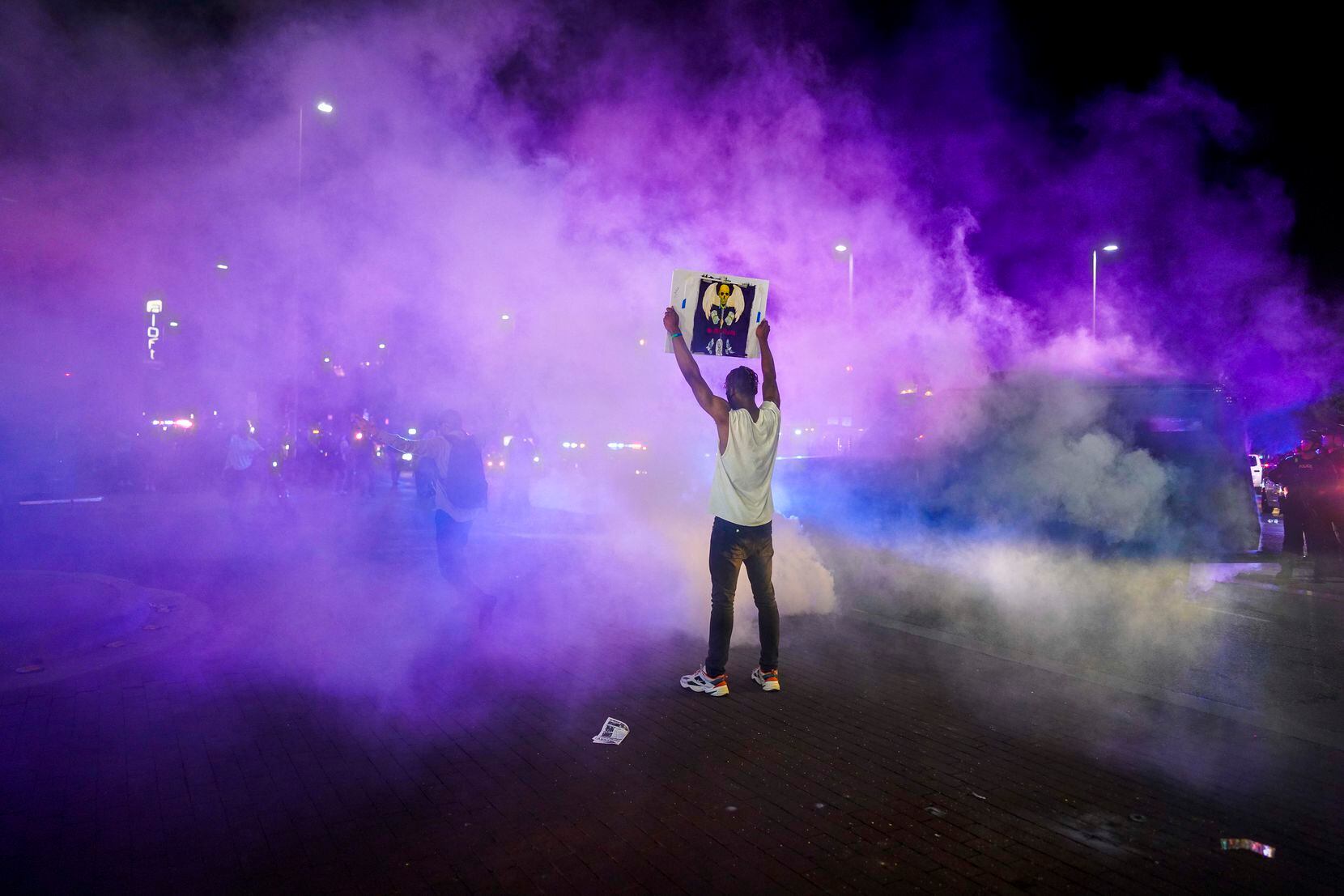 Jordan Spotser holds a sign as Dallas police deploy teargas to disperse protesters at the...