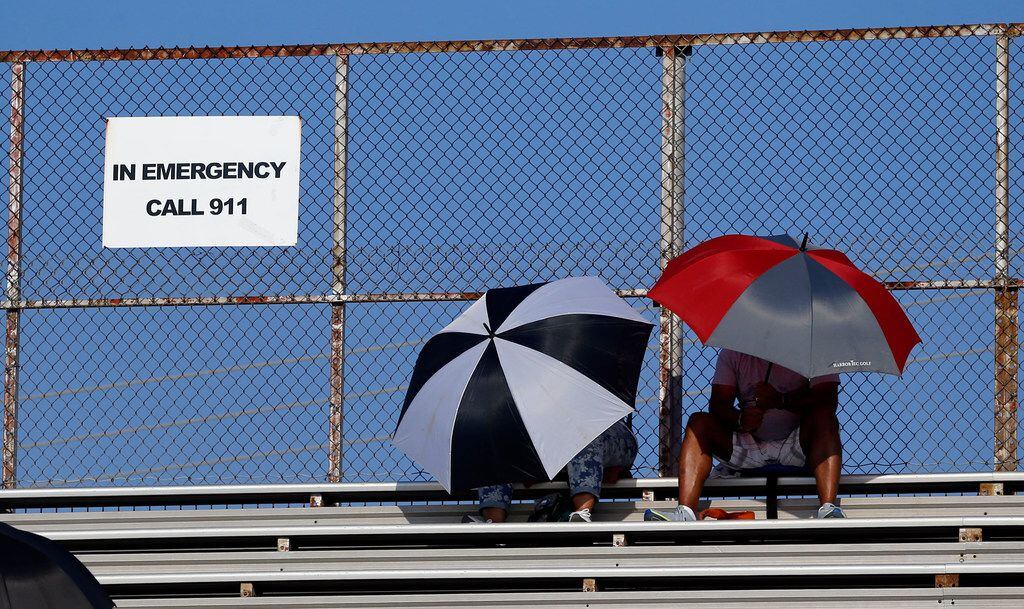 Two fans seek refuge from the heat under umbrellas before the start of the Bishop Dunne...
