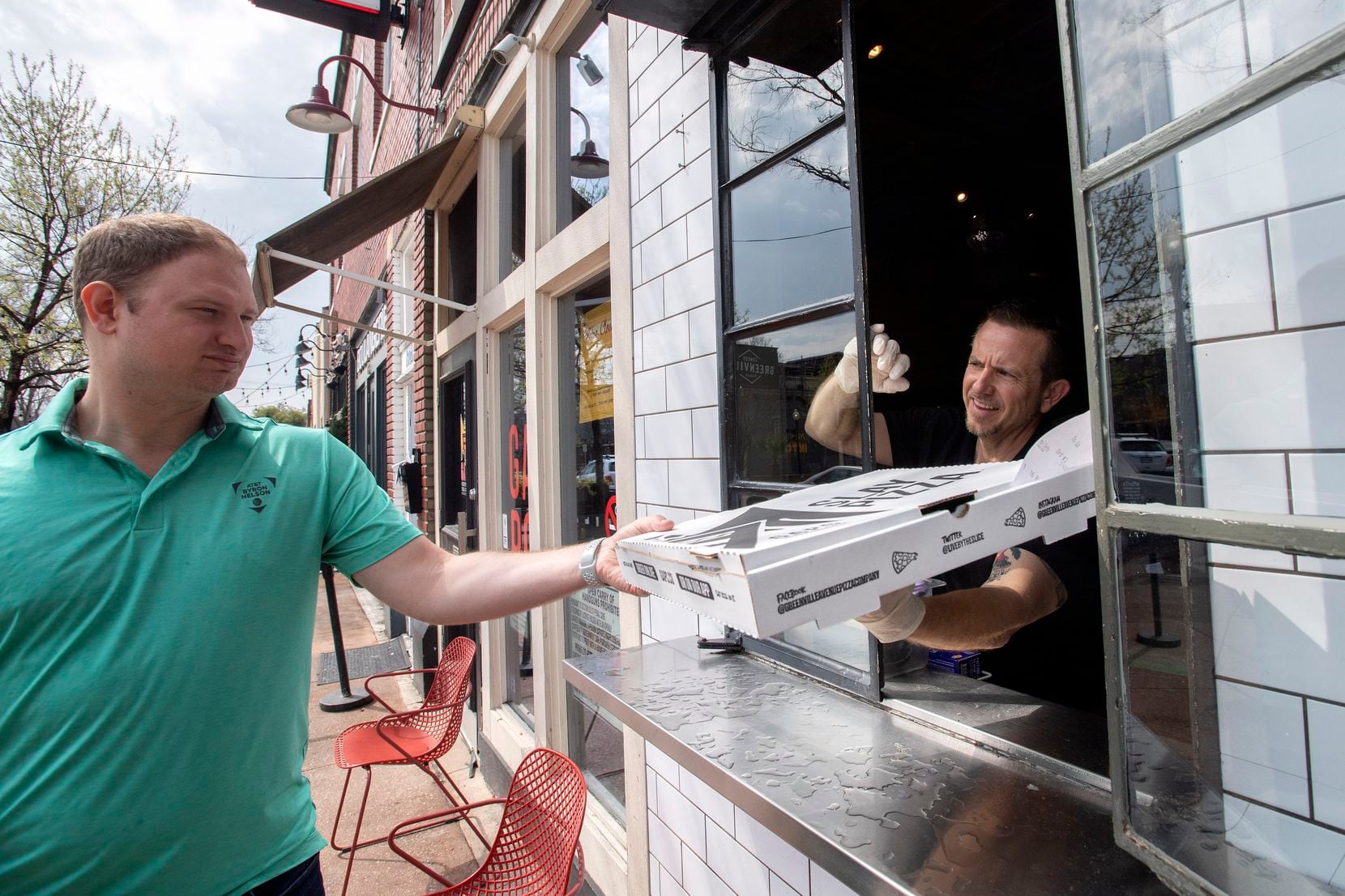 Shelby Wolf, general manager of Greenville Avenue Pizza Company, hands a pick-up order out...