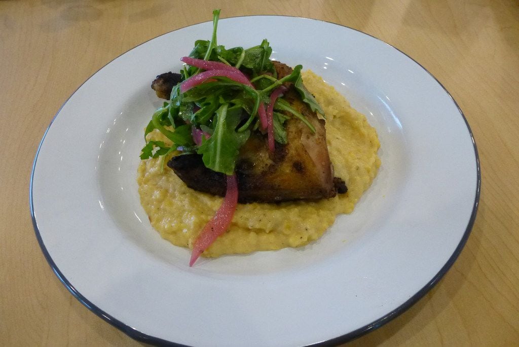 The yardbird and grits at Bonton Farms Cafe includes a charbroiled hind chicken quarter nested on top of rustic Anson Mills grits and garnished with arugula and pickled onions.