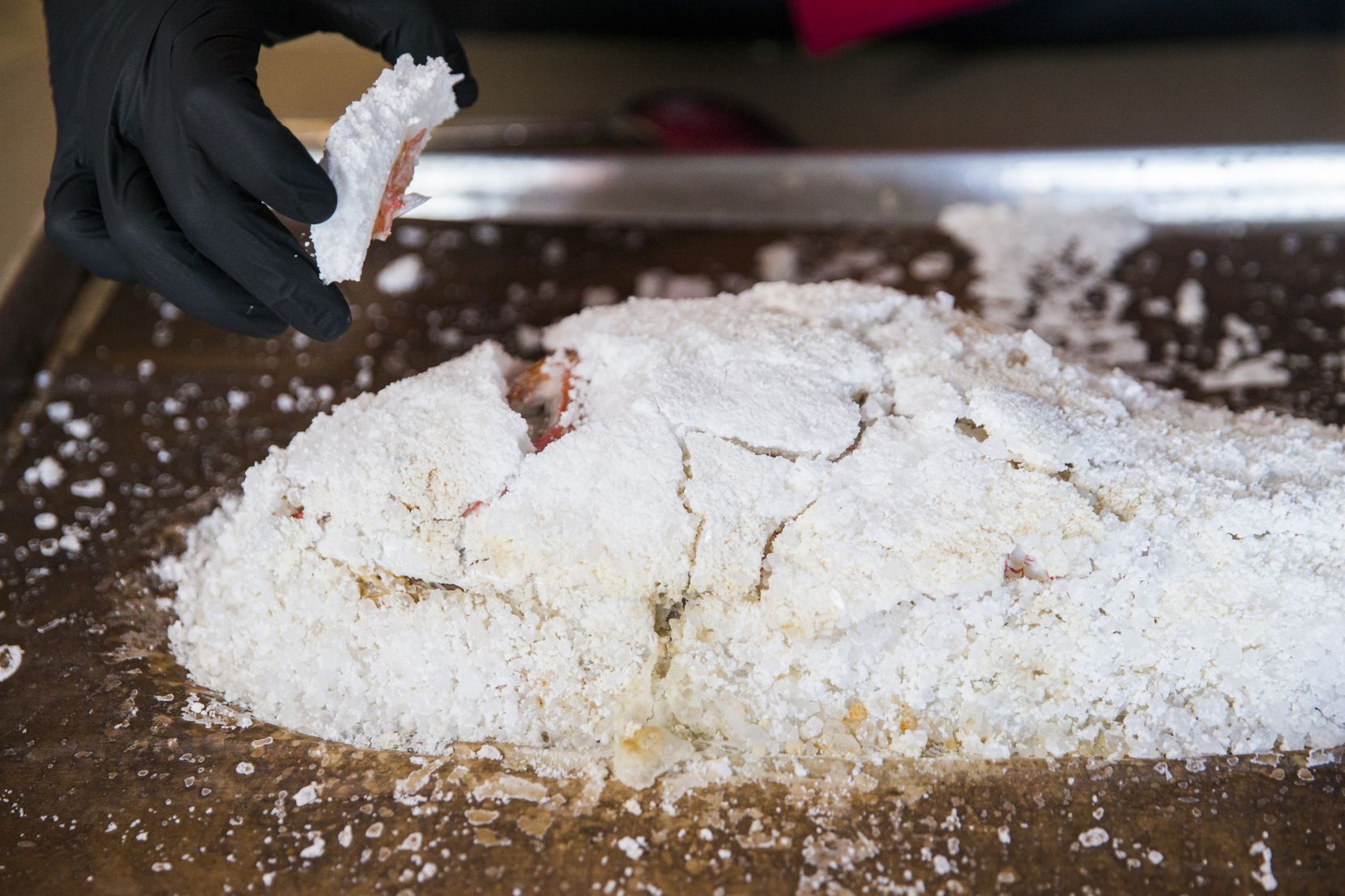 Chef and co-owner Ryan Oruch pulls the salt crust away from the red snapper after baking.