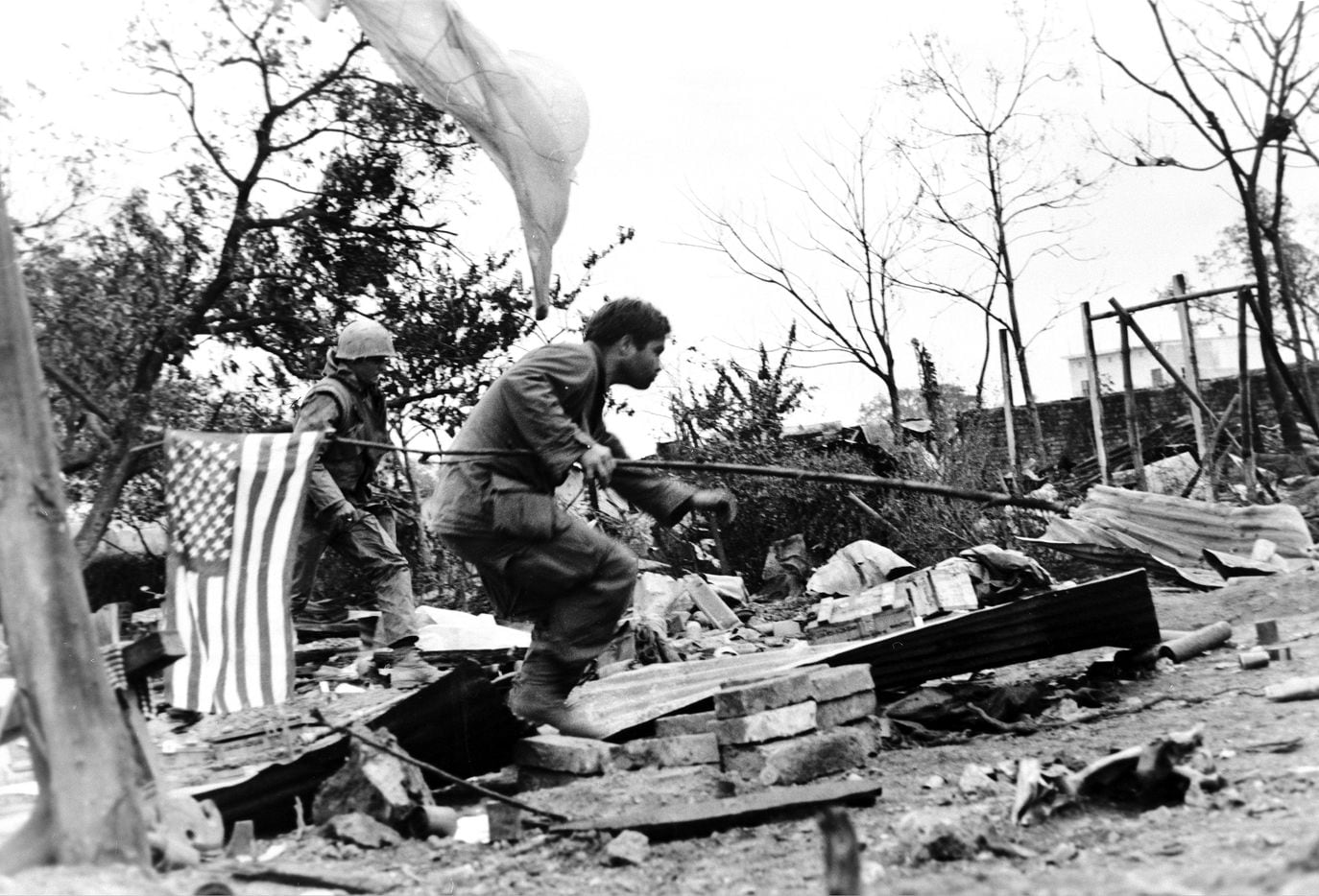 A U.S. Marine carries an American flag as he charges across a rubble-strewn courtyard in the...