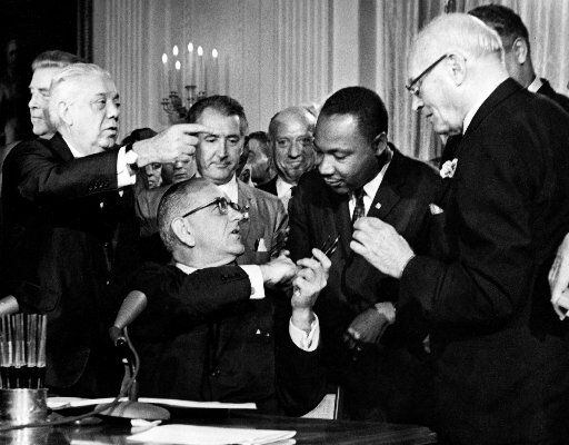 President Lyndon B. Johnson hands a pen to the civil rights leader the Rev. Martin Luther...