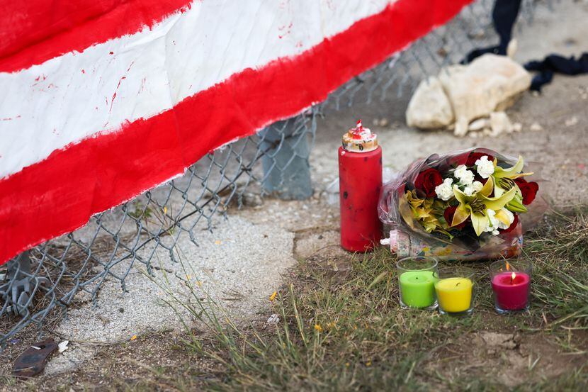 A candle burns near the first bouquet of flowers left at a mural along the fenceline of the...