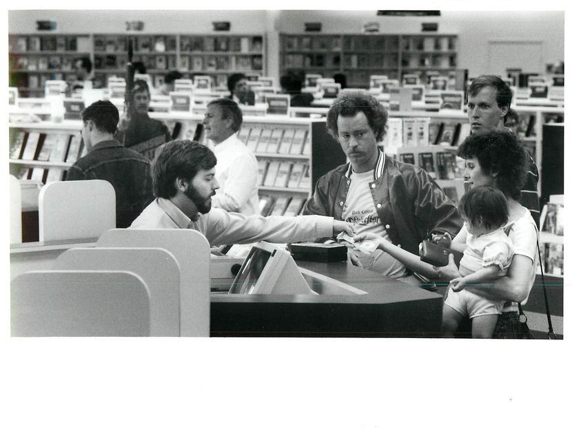 Kirk Denny (left) checks out Cindy Burr and her daughter Tracy, 13 months, at Blockbuster...