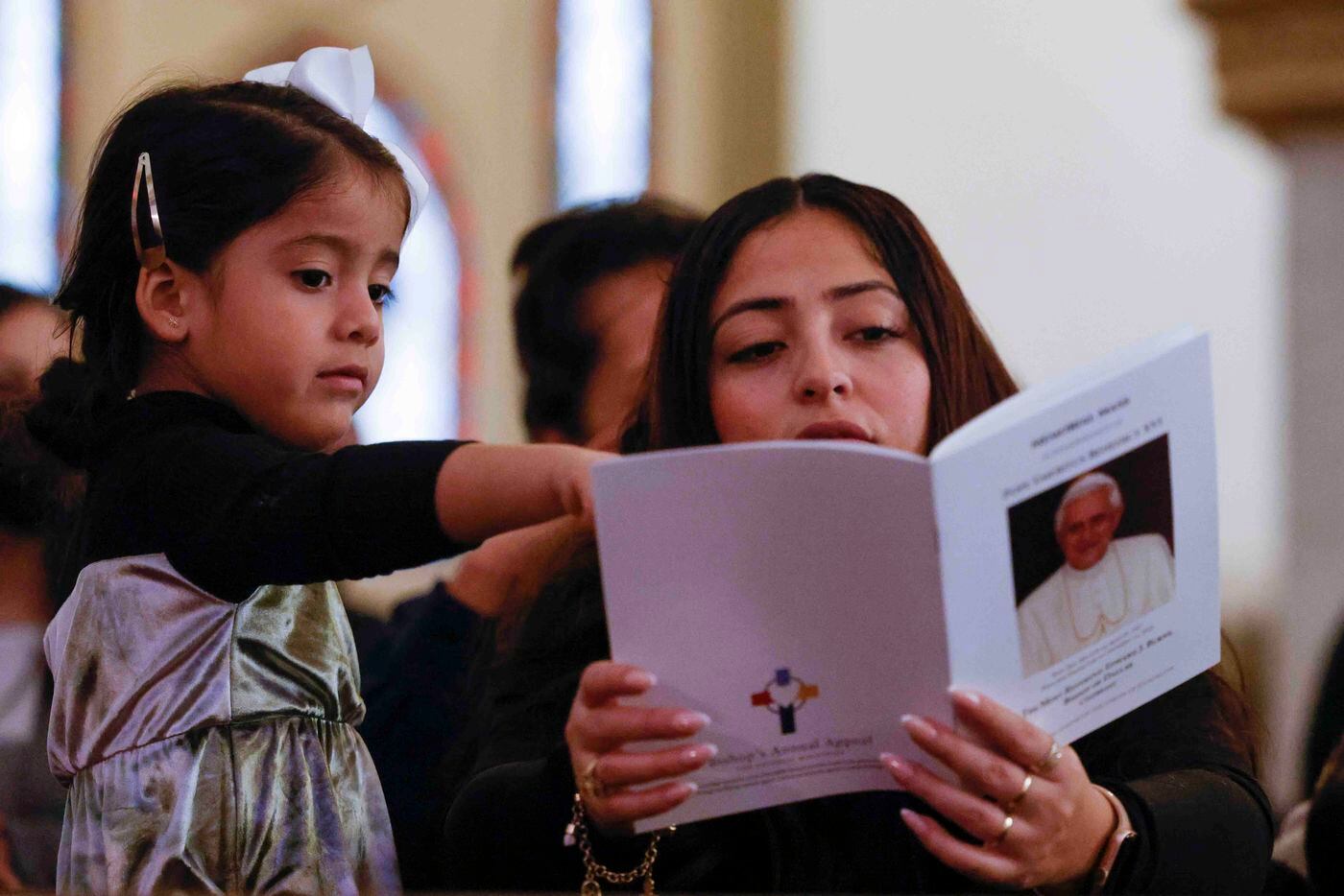 Catalina Nino, 4, points her mother Ana towards the brochure during a memorial mass for late...
