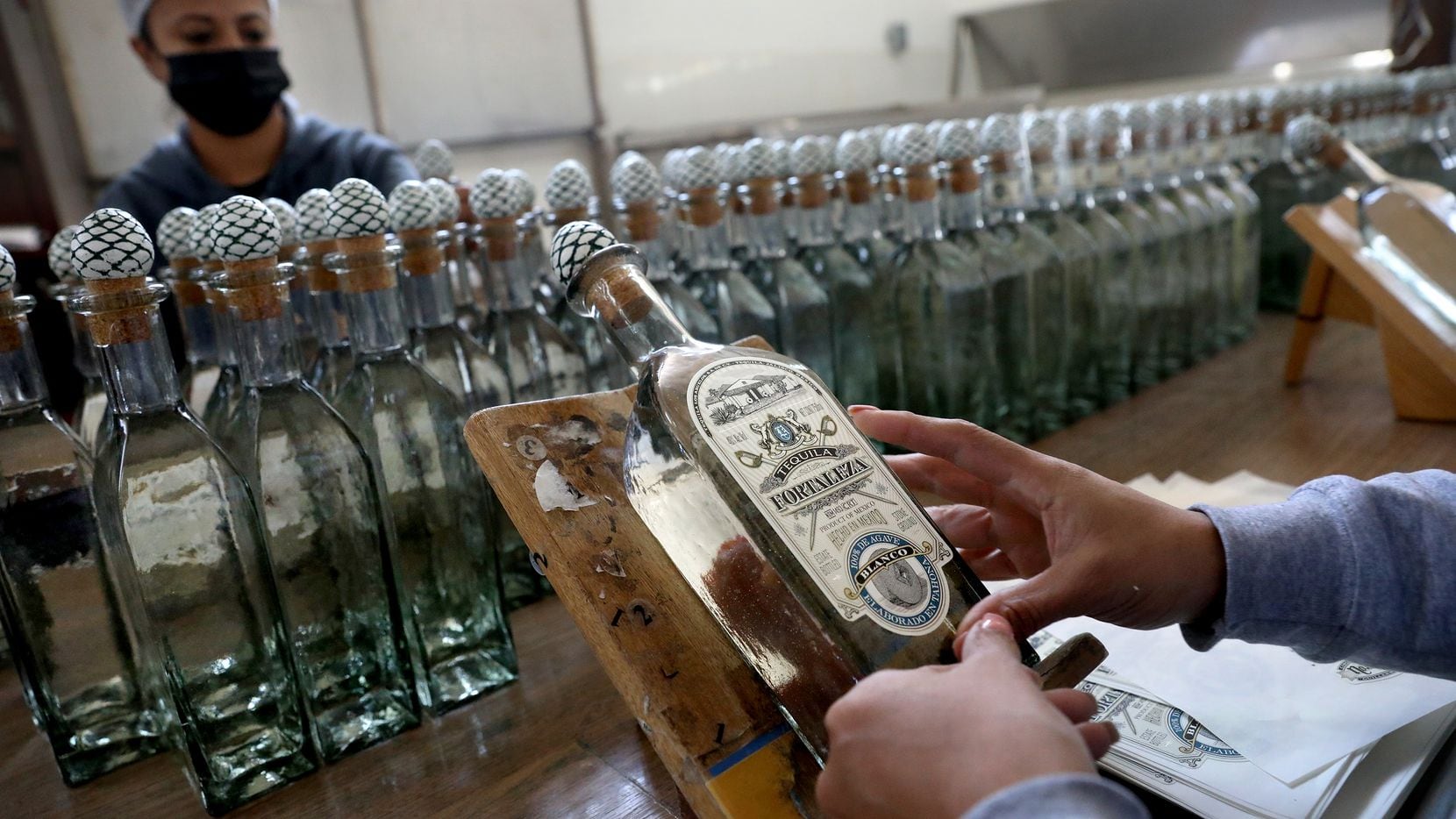 Trabajadores colocan etiquetas a mano en botellas de tequila en la destilería de tequila...
