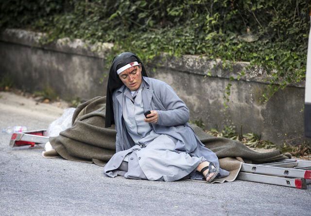 Una monja checa su celular mientras yace junto a una víctima colocada sobre una escalera en...