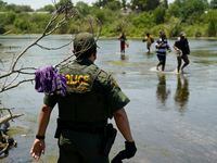 FILE - A Border Patrol agent watches as a group of migrants walk across the Rio Grande on...
