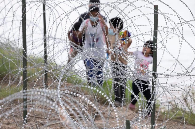 Migrants with children walked by razor wire fencing after crossing the Rio Grande River from...