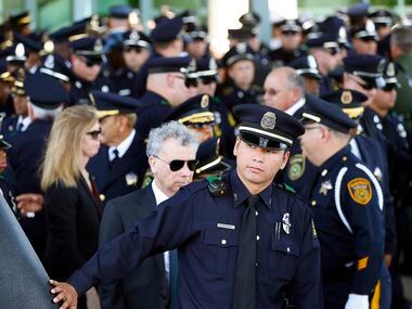 A Dallas police officer runs his hand over the back of the hearse after pallbearers loaded...