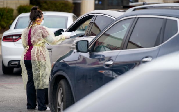 Office manager Kristy Castillo talks with a patient as cars line up for drive-thru...